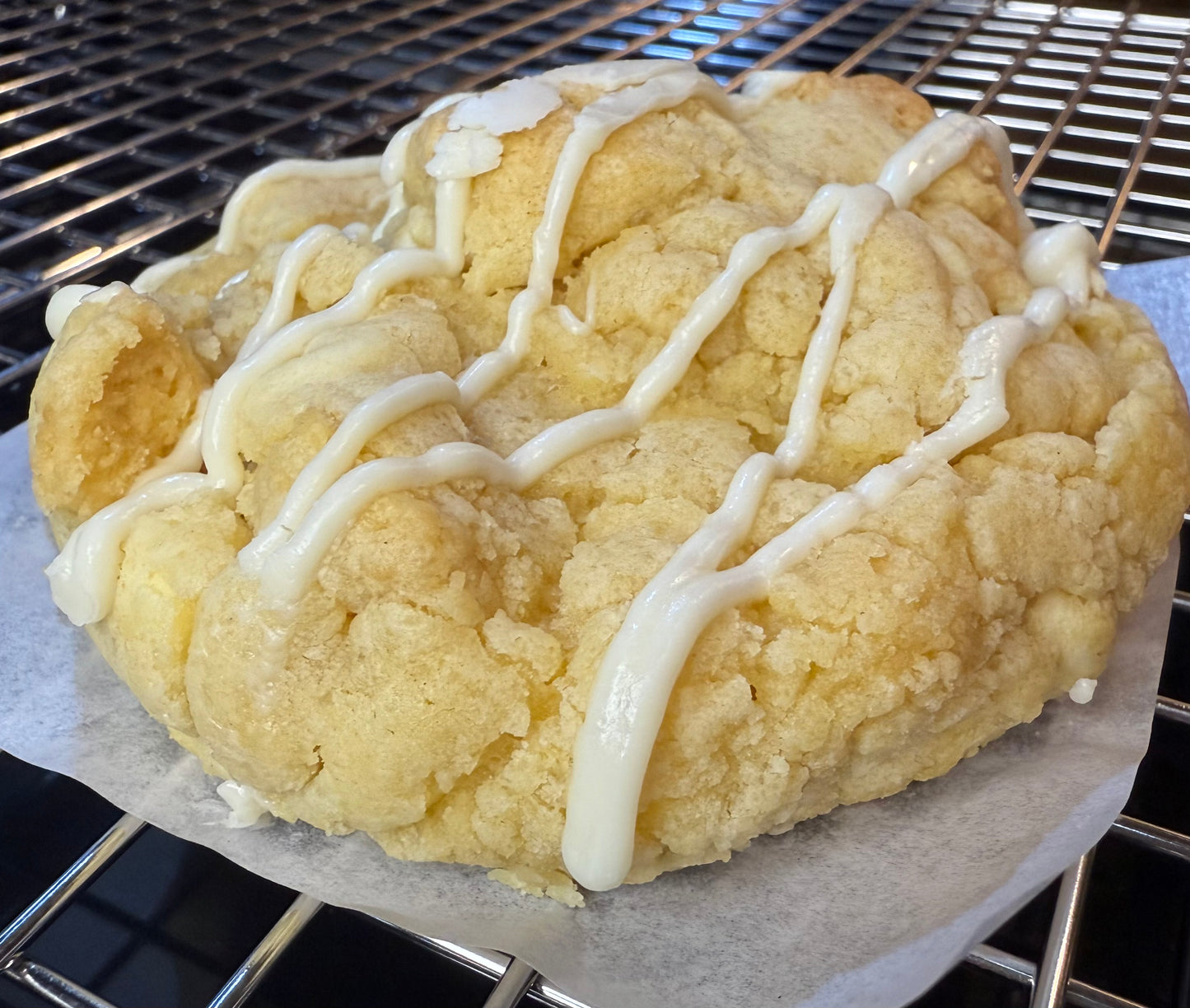 A lemon pudding cookie with white chocolate chips and a drizzle on top, cooling on a wire rack.